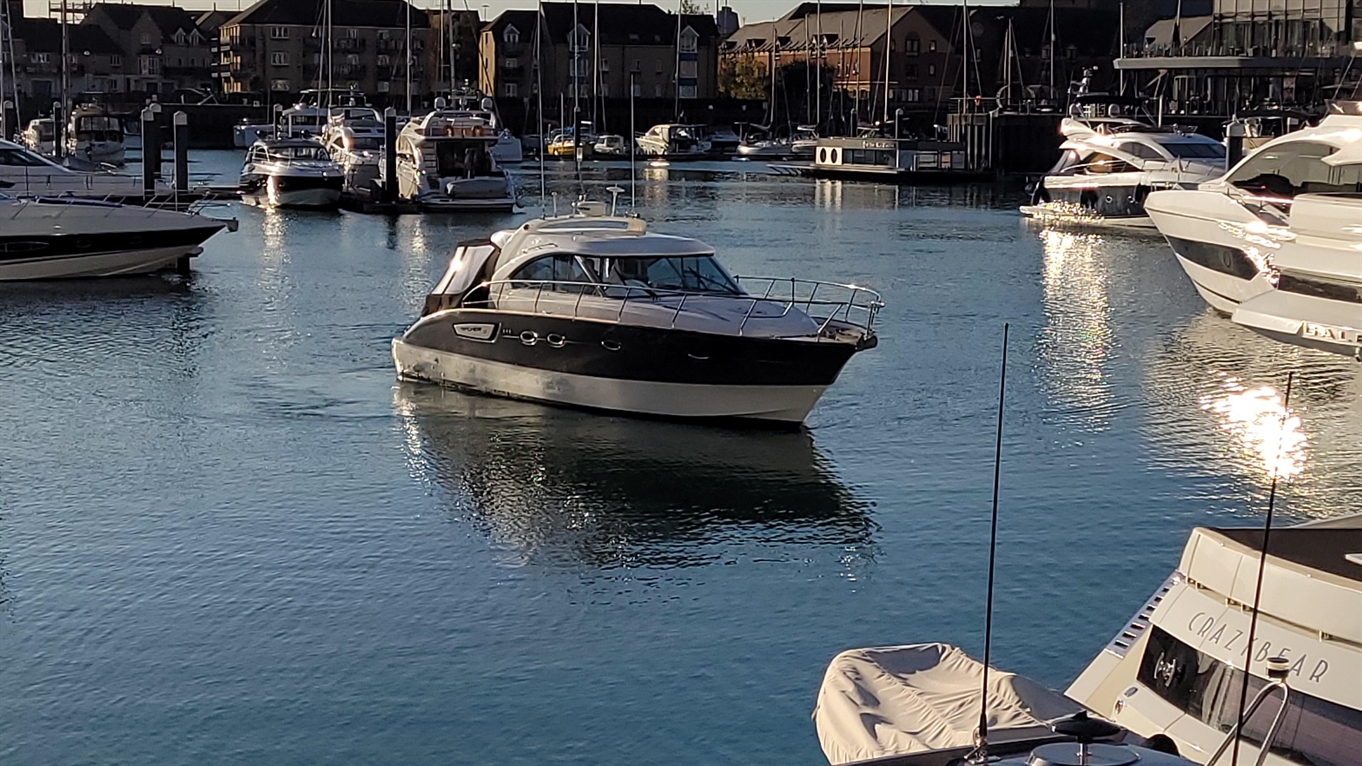 A motorboat navigates a marina filled with yachts and reflections on the water, highlighting a serene evening scene.